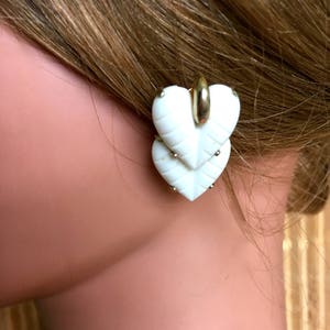 May include: White heart-shaped earrings with a gold-tone metal backing. The earrings are made of two layers of heart-shaped pieces.