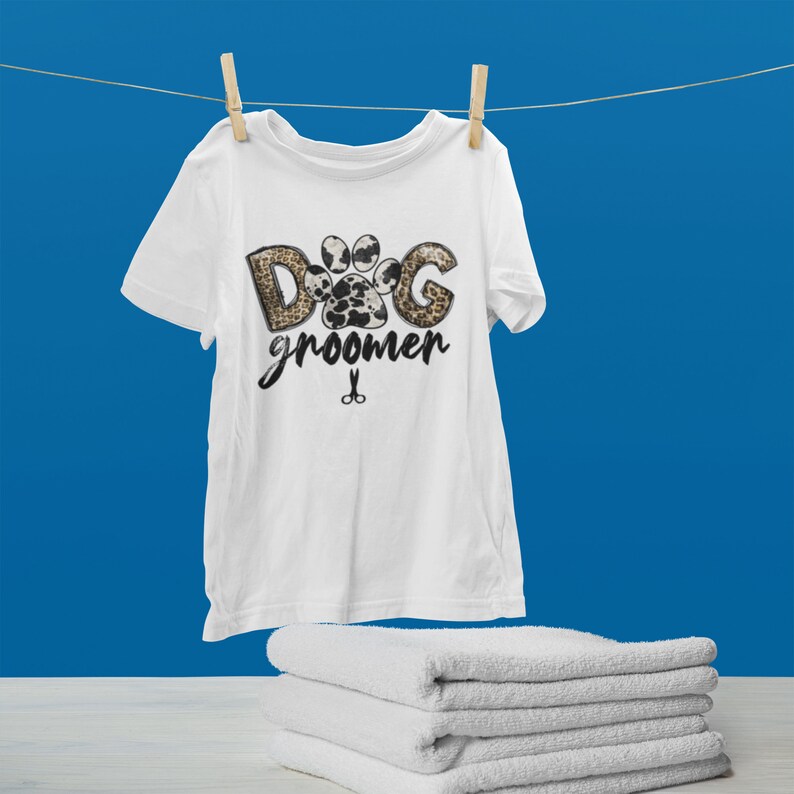 May include: White t-shirt with a paw print design that says "Dog Groomer" with a pair of scissors underneath.