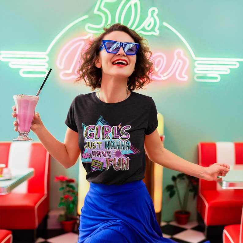May include: A black t-shirt with a retro-style graphic that says "Girls Just Wanna 80s Have Fun". The graphic is in pink, blue, and green with a cassette tape design.