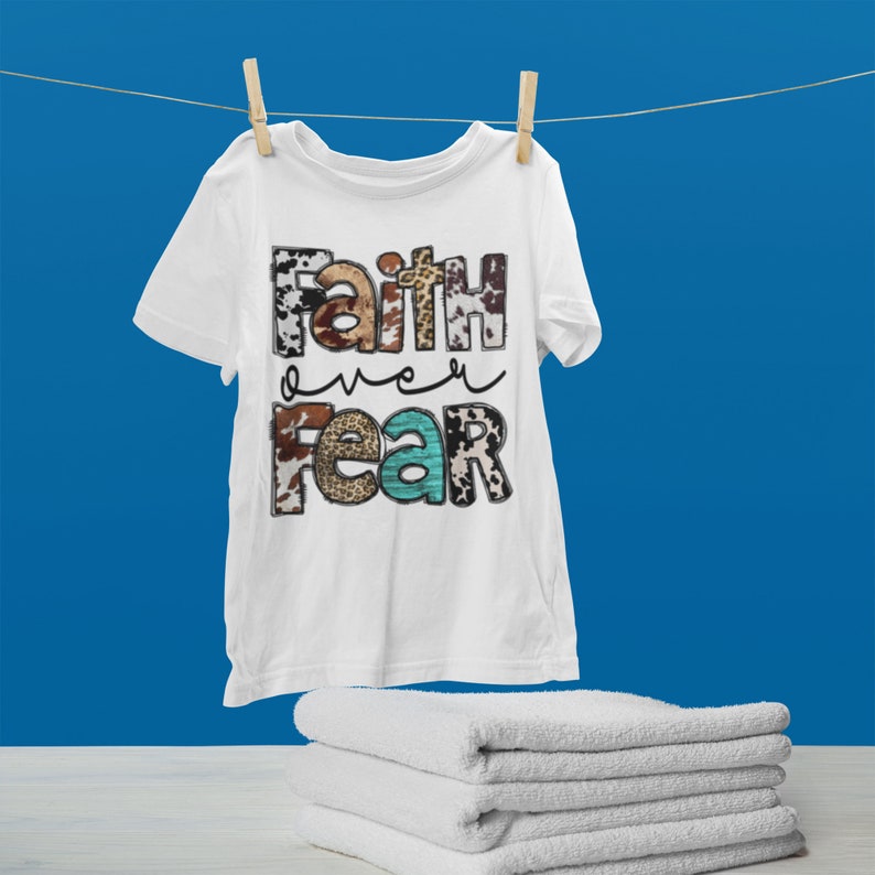 May include: White t-shirt with the text "Faith over Fear" in colorful letters with a cow print pattern.