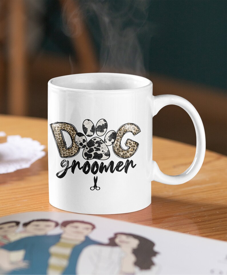 May include: White ceramic mug with a black and brown paw print design. The text "Dog groomer" is written below the paw print. A pair of scissors is below the text.