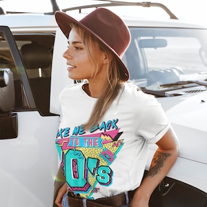 May include: A white t-shirt with a retro 80s graphic design featuring the text "Take Me Back To The 80s" in a colorful, geometric style. The design includes a cassette tape and a pink and blue color scheme.