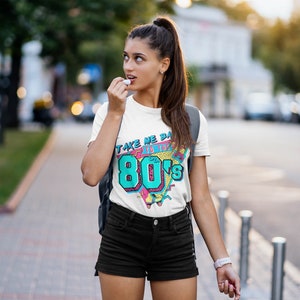 May include: White t-shirt with a graphic print of a retro 80s design. The graphic features the text "Take Me Back to the 80's" with a colorful geometric pattern.