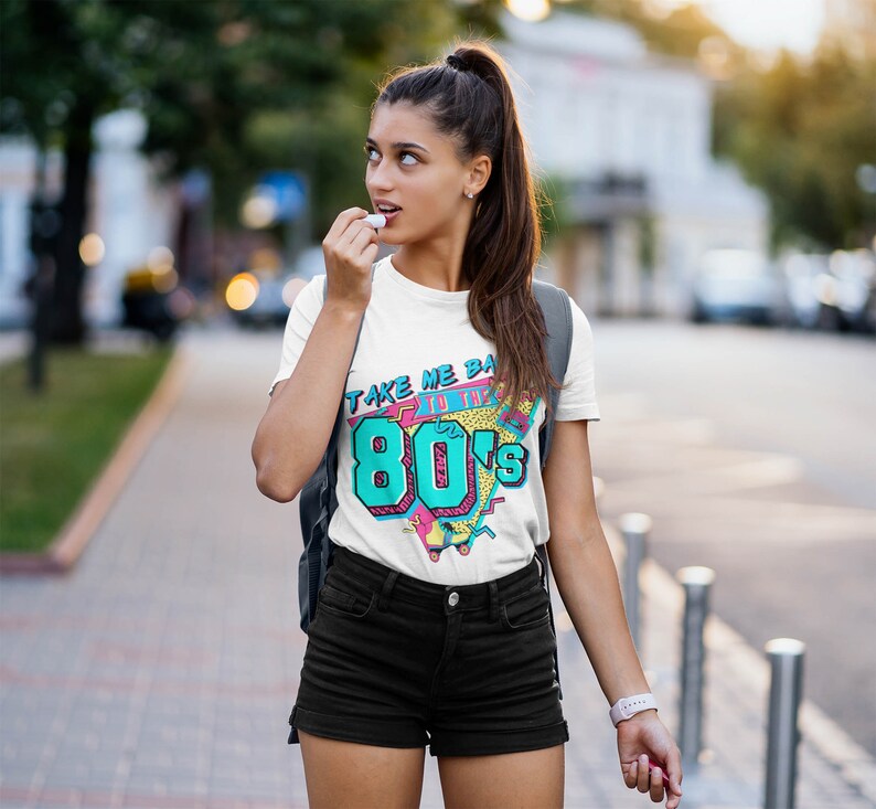 May include: White t-shirt with a graphic print of a retro 80s design. The graphic features the text "Take Me Back to the 80's" with a colorful geometric pattern.