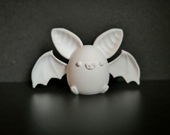 Könnte beinhalten: Eine weiße, 3D-gedruckte Fledermausfigur mit großen Ohren und Flügeln. Die Fledermaus hat einen abgerundeten Körper, kleine Füße und ein lächelndes Gesicht. Die Figur steht vor einem dunklen Hintergrund.