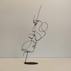 Può includere: Scultura in metallo nero raffigurante due volti in uno stile di arte lineare continua. La scultura è montata su una piccola base rotonda. I volti sono di profilo, uno leggermente sopra l'altro, suggerendo un abbraccio o un bacio.