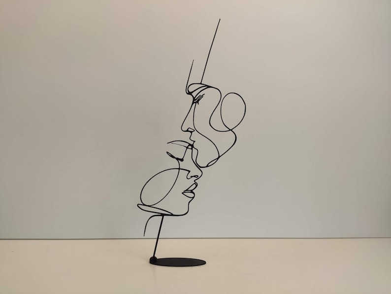 Peut inclure: Sculpture en m&eacute;tal noir repr&eacute;sentant deux visages en style de dessin au trait continu. La sculpture est mont&eacute;e sur une petite base ronde. Les visages sont de profil, l'un au-dessus de l'autre, sugg&eacute;rant une &eacute;treinte ou un baiser.
