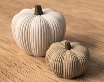 May include: Two decorative pumpkins, one large and one small, sit on a wooden surface. The larger pumpkin is off-white, while the smaller one is tan. Both have ribbed textures and dark green stems, perfect for fall decor.