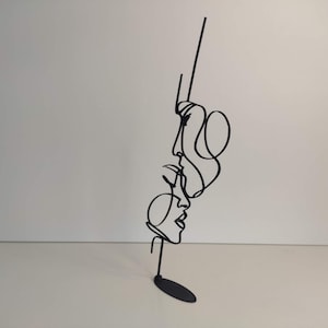 Peut inclure: Sculpture en m&eacute;tal noir repr&eacute;sentant trois visages en une ligne continue. L'&oelig;uvre pr&eacute;sente un design minimaliste avec une petite base ronde. Les visages sont de profil, avec des lignes fluides repr&eacute;sentant les cheveux et les traits du visage. Un objet de d&eacute;coration moderne.