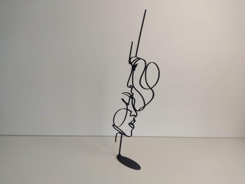 Peut inclure: Sculpture en m&eacute;tal noir repr&eacute;sentant trois visages en une ligne continue. L'&oelig;uvre pr&eacute;sente un design minimaliste avec une petite base ronde. Les visages sont de profil, avec des lignes fluides repr&eacute;sentant les cheveux et les traits du visage. Un objet de d&eacute;coration moderne.