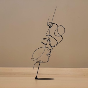 Peut inclure: Sculpture en m&eacute;tal noir repr&eacute;sentant deux visages dans un style d'art en ligne continue. L'&oelig;uvre d'art est mont&eacute;e sur une petite base rectangulaire, cr&eacute;ant une esth&eacute;tique minimaliste et moderne. La sculpture est une pi&egrave;ce d&eacute;corative.
