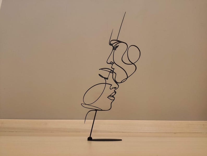 Peut inclure: Sculpture en m&eacute;tal noir repr&eacute;sentant deux visages dans un style d'art en ligne continue. L'&oelig;uvre d'art est mont&eacute;e sur une petite base rectangulaire, cr&eacute;ant une esth&eacute;tique minimaliste et moderne. La sculpture est une pi&egrave;ce d&eacute;corative.