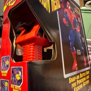 Puede incluir: Una figura de acci&oacute;n electr&oacute;nica de Spider-Man en caja. El embalaje es rojo y negro, con las palabras "Electronic Action Hero" en amarillo. La caja presenta im&aacute;genes de la figura en acci&oacute;n, con texto que dice "Punching Action!", "Real Battle Sound Effect!" y "Kicking Action!"