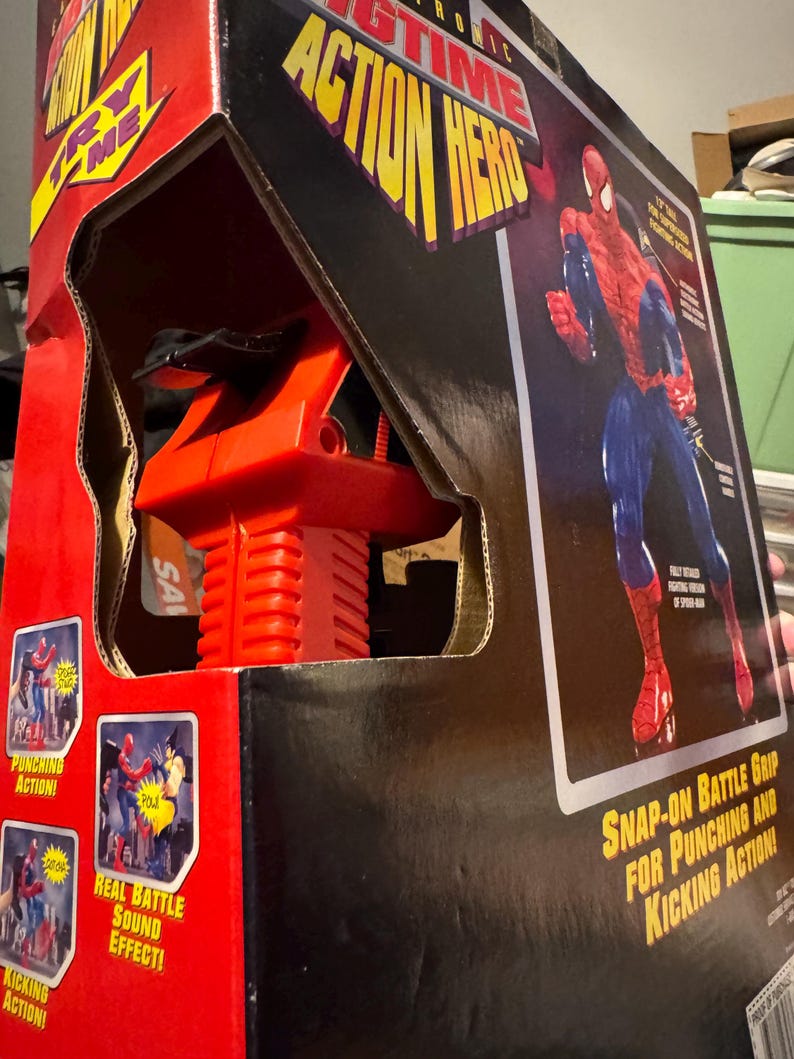 Puede incluir: Una figura de acci&oacute;n electr&oacute;nica de Spider-Man en caja. El embalaje es rojo y negro, con las palabras "Electronic Action Hero" en amarillo. La caja presenta im&aacute;genes de la figura en acci&oacute;n, con texto que dice "Punching Action!", "Real Battle Sound Effect!" y "Kicking Action!"