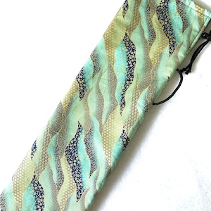 Può includere: Astuccio in tessuto con chiusura a coulisse, caratterizzato da un motivo a onde ripetuto nei toni del verde acqua, oro e blu navy. Il design incorpora varie trame e accenti floreali. L'astuccio è probabilmente progettato per contenere un oggetto lungo e sottile.