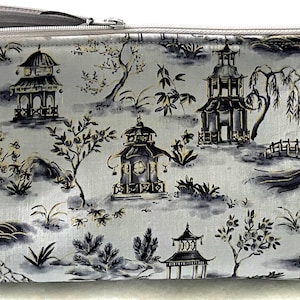 May include: A grey zippered pouch with a white background and a black and white pattern of Japanese pagodas, trees, and bridges.