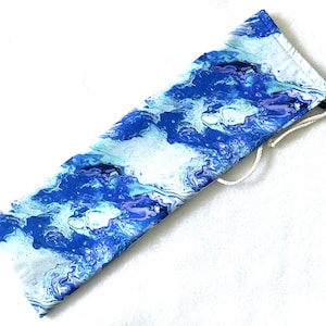 May include: A fabric case with a blue and white marbled pattern. The case is rectangular with a drawstring closure. The design resembles ocean waves, with shades of blue, white, and hints of purple. The case is likely for storing items.