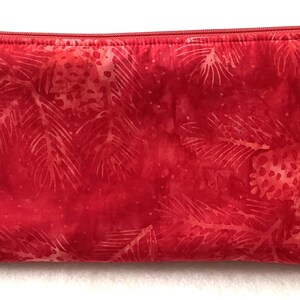 May include: A rectangular red fabric pencil case featuring a tonal print of pine branches and pinecones. The case has a matching red zip closure along the top edge, providing a secure opening for storing various small items and stationery.