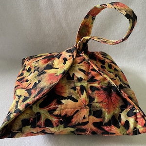 Op de afbeelding: Een gevoerde stoffen tas met een zwarte achtergrond en een patroon van kleurrijke herfstbladeren. De tas heeft een enkele lusvormige handgreep.