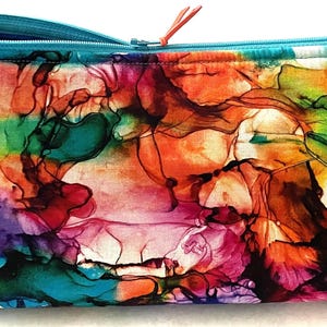 Può includere: Un astuccio rettangolare con cerniera e un vivace design astratto. Il motivo presenta una miscela di colori tra cui rosso, arancione, verde, blu e viola. La cerniera e il bordo sono di un turchese brillante e il tirazip è arancione.