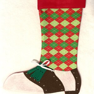 May include: A red and green argyle stocking with a brown and white felt shoe at the toe. The shoe has green laces and a white tassel.
