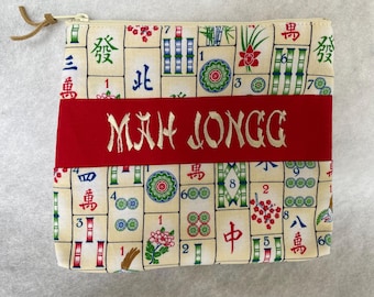 Op de afbeelding: Een rode ritszak met een witte achtergrond en een Mahjong-ontwerp. De tas heeft een rode band met de woorden "MAH JONGG" geborduurd in gouden draad.