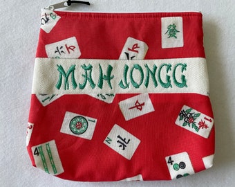 May include: Red zippered pouch with a white band that says "MAH JONGG" in green embroidery. The pouch is covered in a pattern of white mahjong tiles with green and black characters.