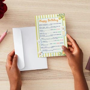 May include: A birthday card with a green and white striped background and the words "Happy Birthday" in orange. The card has a floral design and is held with a white envelope. The card includes prompts for filling in details.