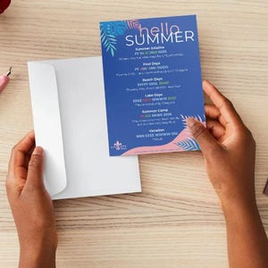 May include: A blue and pink summer-themed card with the words "hello SUMMER" in white. The card is held next to a white envelope. The card lists summer events and dates. The background is a light wood color.