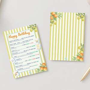 May include: Two birthday-themed cards with a yellow and white striped pattern. One card has the text "Happy Birthday" and other details. Both cards feature watercolor illustrations of oranges and lemons. A gold pen rests nearby.