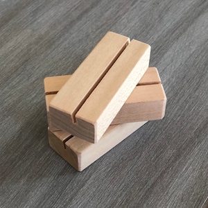 May include: Two wooden display stands with a slot in the center for holding cards or signs. The stands are made of natural wood and are stacked on top of each other.