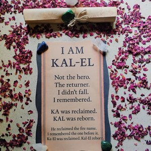 May include: A beige scroll tied with twine, sealed with a green stone, and surrounded by dried rose petals. A tan paper with the text "I AM KAL-EL" and other text is in the center, with various crystals scattered around.