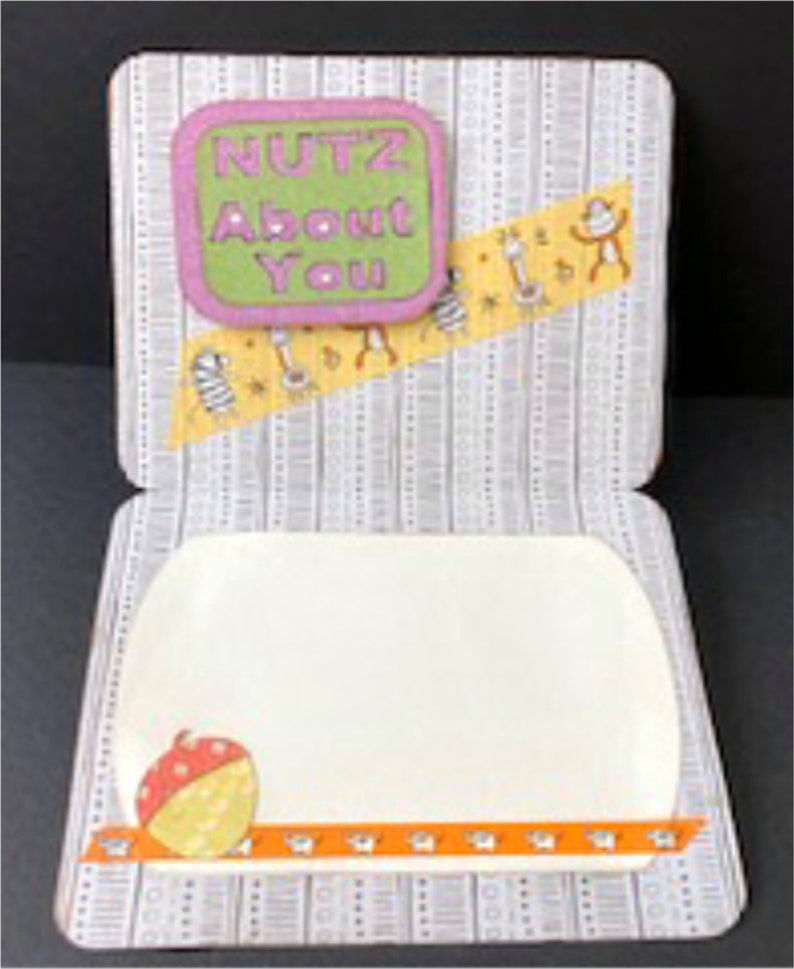 May include: A white card with a grey and white patterned background. The card is folded in half and has a small, green and pink square with the text "NUTZ ABOUT YOU" on the front. The inside of the card is blank.