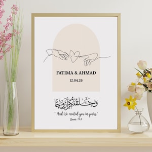 Op de afbeelding: Een ingelijste wandprint met een zwarte lijntekening van twee handen die naar een hart reiken, tegen een beige boog. Het bevat de tekst FATIMA & AHMAD, de datum 12.04.26, en Arabische kalligrafie met de Engelse tekst And We created you in pairs. Quran 78:8.