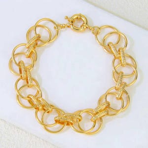 May include: A gold-toned chain bracelet composed of interlocking circular links. Several of the links feature a textured, sparkling surface, while others are smooth and polished. The bracelet is secured with a round spring-ring clasp.