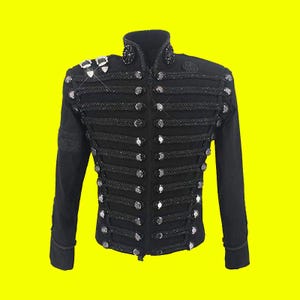 May include: Black military-style jacket with a high collar and decorative rope trim. The jacket features rows of silver-colored buttons and embellishments on the shoulders and collar. The long-sleeved jacket is a formal style.