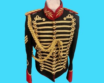 May include: Black military jacket with gold braid and buttons. The jacket has a red collar and cuffs, and gold epaulets. The jacket is displayed on a mannequin against a blue background. The jacket has a high collar and a double row of buttons.