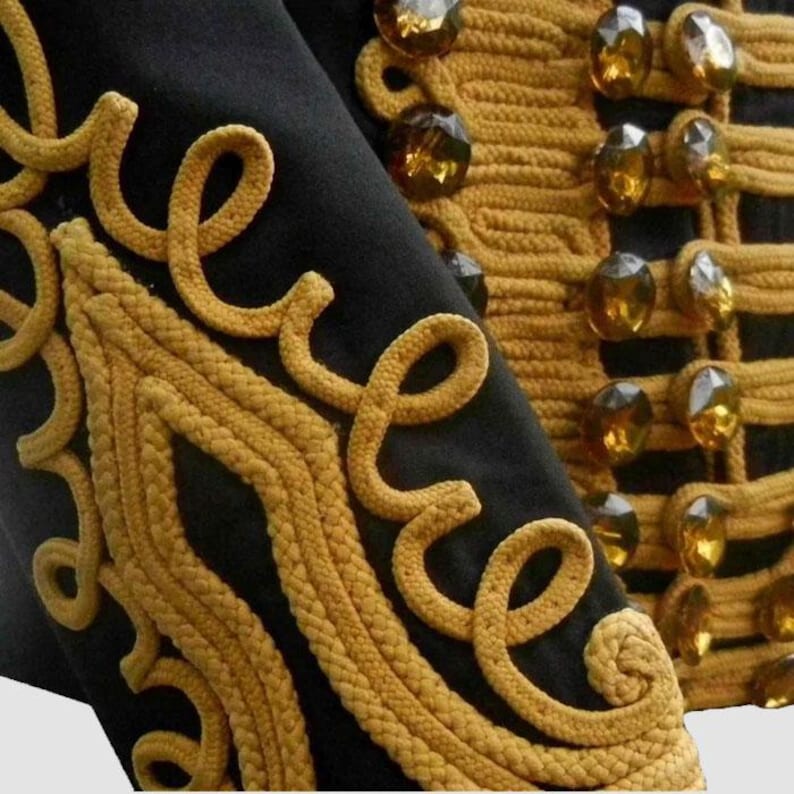 May include: Close-up of a black jacket with ornate gold rope embroidery and decorative amber-colored buttons. The gold rope detailing forms intricate patterns along the edges and seams, creating a luxurious and detailed appearance.