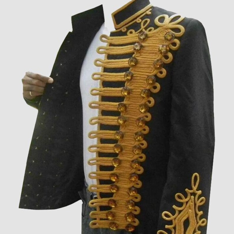 May include: Black military-style jacket with gold-colored trim and decorative buttons. The jacket features ornate gold embroidery on the shoulder and sleeve. The jacket is open, revealing a white shirt underneath.