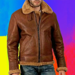 Puede incluir: Chaqueta de cuero marrón con cuello y ribetes de borrego. La chaqueta tiene cremallera frontal, bolsillo en el pecho y parche en la manga izquierda. La chaqueta se lleva sobre una camisa blanca y vaqueros azules. El fondo es un degradado de colores.