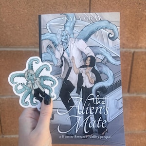 May include: A paperback book titled The Alien's Mate by Skyla Gray, featuring an illustration of a pale blue tentacled creature and a person in a lab coat, accompanied by a matching die-cut sticker of the same tentacled character design.