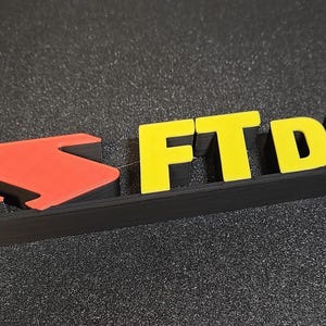May include: A black, red, and yellow sign with the text "FT DX10". The yellow letters "FT DX10" are prominent against the black base. The sign also features a red arrow-like design.