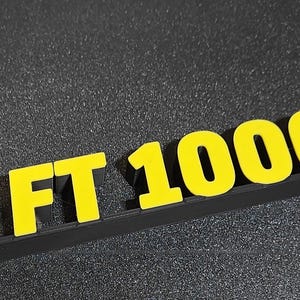 May include: A black and red logo featuring the letters "S" and "FT 1000 MP" in yellow. The logo is on a black surface. The "S" is red, and the letters "FT 1000 MP" are yellow.