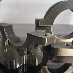 Op de afbeelding: Close-up van verschillende zwarte 3D-geprinte componenten. De onderdelen hebben een matte afwerking en hebben geometrische vormen, waaronder gebogen en rechthoekige elementen. De componenten lijken te zijn ontworpen voor mechanische of structurele toepassingen, met gaten voor bevestigingsmiddelen.