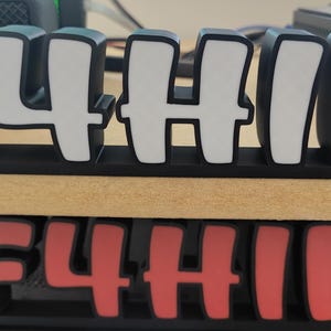 May include: A black and white desktop sign spelling "F4HIK". The letters are white with a black outline and base. A second sign with the same design is visible below, in red and white.