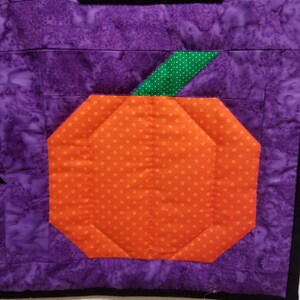 May include: A purple and orange patchwork quilt block featuring a pumpkin design. The pumpkin is orange with white polka dots and has a green stem with white polka dots.