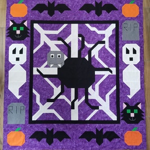 May include: Purple fabric with a black spider web design. The web has a black spider in the centre. There are black bats, orange pumpkins, and grey tombstones with the word "RIP" on them around the web.