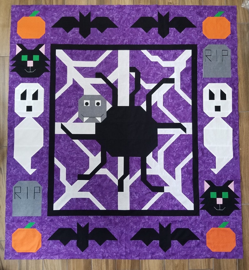 May include: Purple fabric with a black spider web design. The web has a black spider in the centre. There are black bats, orange pumpkins, and grey tombstones with the word "RIP" on them around the web.
