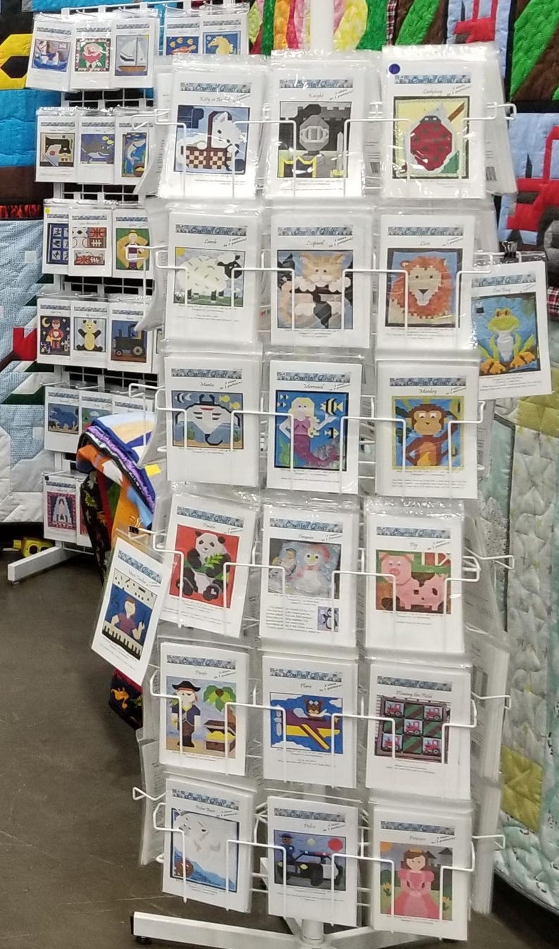 May include: A white metal display stand with multiple rows of colorful printed fabric squares. Each square features a different design, including animals, people, and objects. The designs are all in a pixelated style, reminiscent of cross-stitch or embroidery.