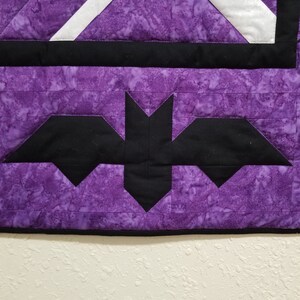 May include: Purple and black quilt with a bat design. The quilt is made of fabric with a marbled pattern.